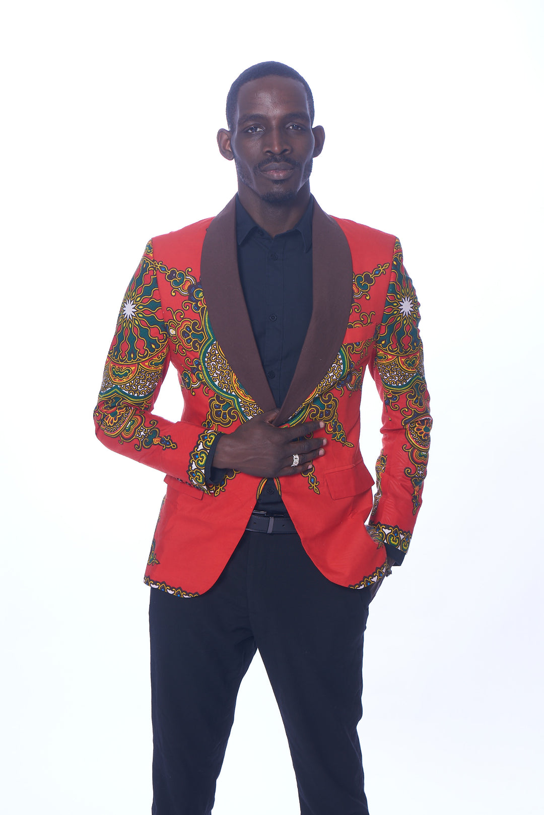 Photo of a man wearing myObioma's red Dashiki Blazer. It features beautiful green and yellow geometric patterns that loop around the sleeves and dark lapels. Classic red flap pockets are included on each side for usage and subtlety as they blend perfectly into the blazer.