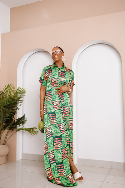 Woman in a green patterned dress standing in a room with arches and a plant.