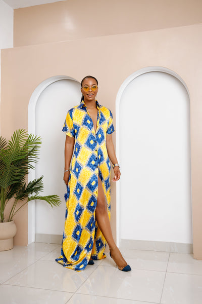 Woman wearing a yellow and blue patterned dress standing in a room with arches and a plant.