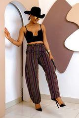Woman in a stylish outfit with a black top and striped pants, standing against a modern interior background.