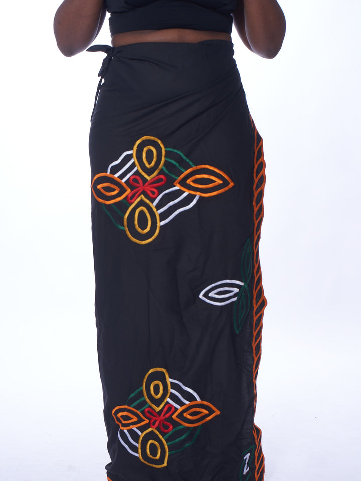 Photo of a woman wearing myObioma's Gelila Ethiopian Skirt, which is long and black. The wrap-around skirt includes multicolor flower-like patterns.