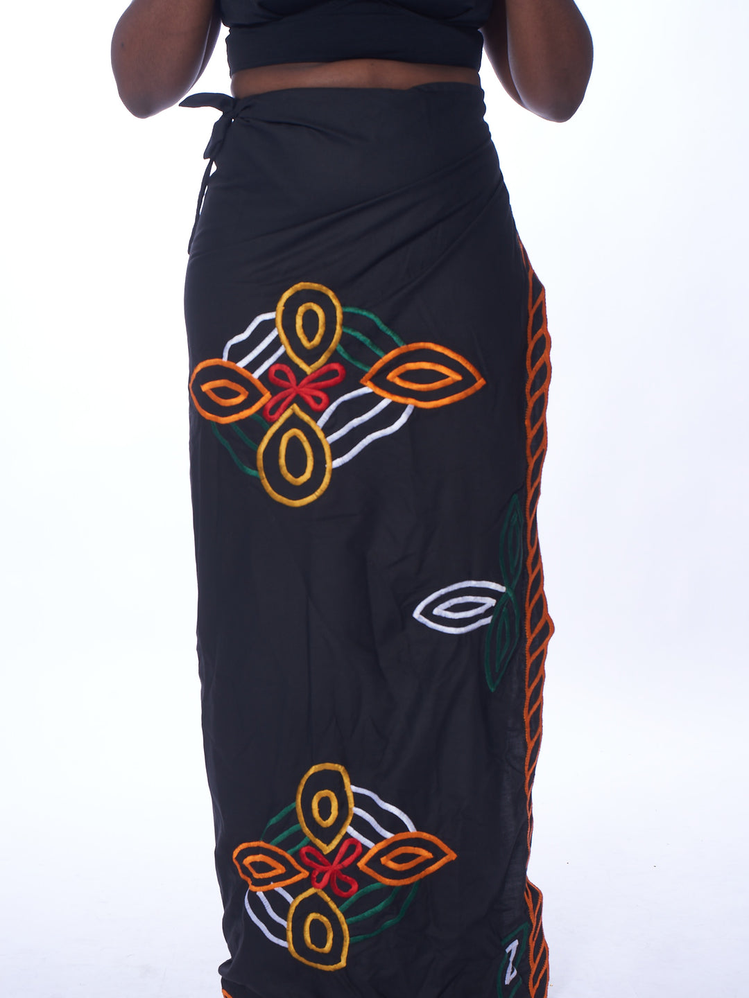 Photo of a woman wearing myObioma's Gelila Ethiopian Skirt, which is long and black. The wrap-around skirt includes multicolor flower-like patterns.