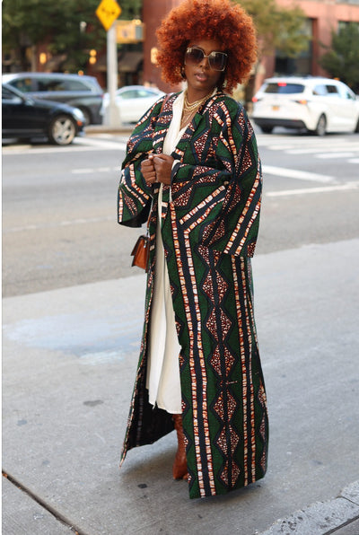 Photo of a woman wearing myObioma’s Aziza Kimono, which is a dark green full-length kimono robe. The long, open-front kimono is loose and lightweight with long and loose sleeves. The robe also has attractive multicolor geometric prints that add vibrance. 