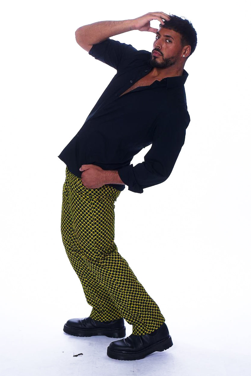 Photo of a man wearing my Obioma's slim-fit pants. The patterned pants feature geometric yellow and black prints, which are scaled to feel like a lavish texture. They also include patterned pockets that blend with the pants for convenience and subtlety.
