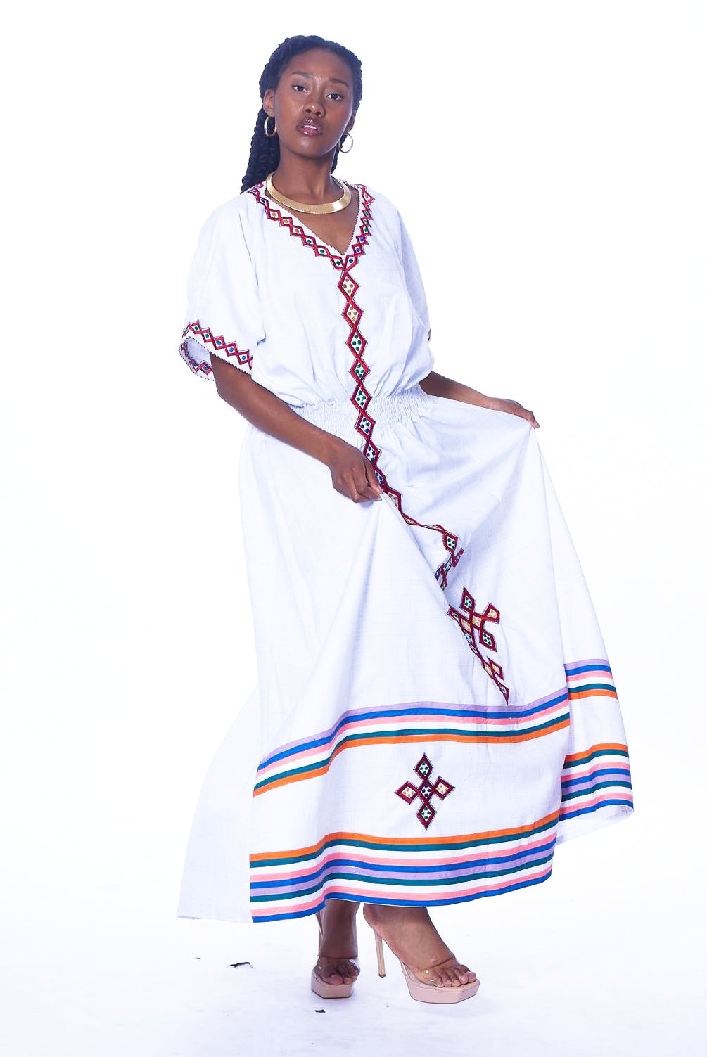 Photo of a woman wearing myObioma's Salem Dress, which is white and long. The v-neck dress features embroidered geometric diamonds and lines from the collar to the hem.