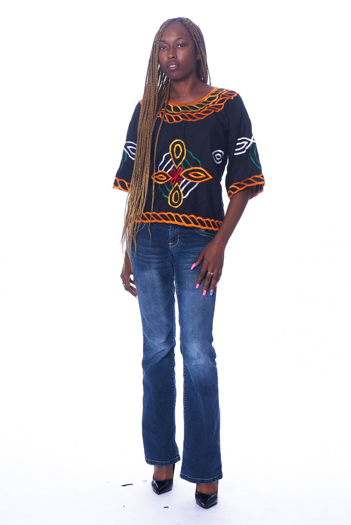 Photo of a woman wearing myObioma's Desta Shirt, which is black and includes a large multicolor flower-like embroidery design in the center. The round-neck shirt has medium-length sleeves for comfort.