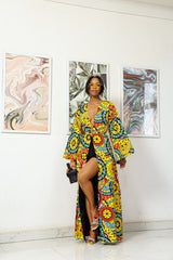 A woman wearing a colorful traditional African ankara fabric kimono, standing in front of abstract art paintings.