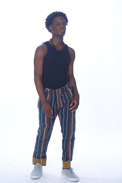 Photo of a man wearing myObioma's multicolor and straight-legged Trad Sankara Pants. The pants are filled with dark vertical patterns bring an edgy aspect to the otherwise incredibly casual pants. The hem features thick yellow horizontal lines.