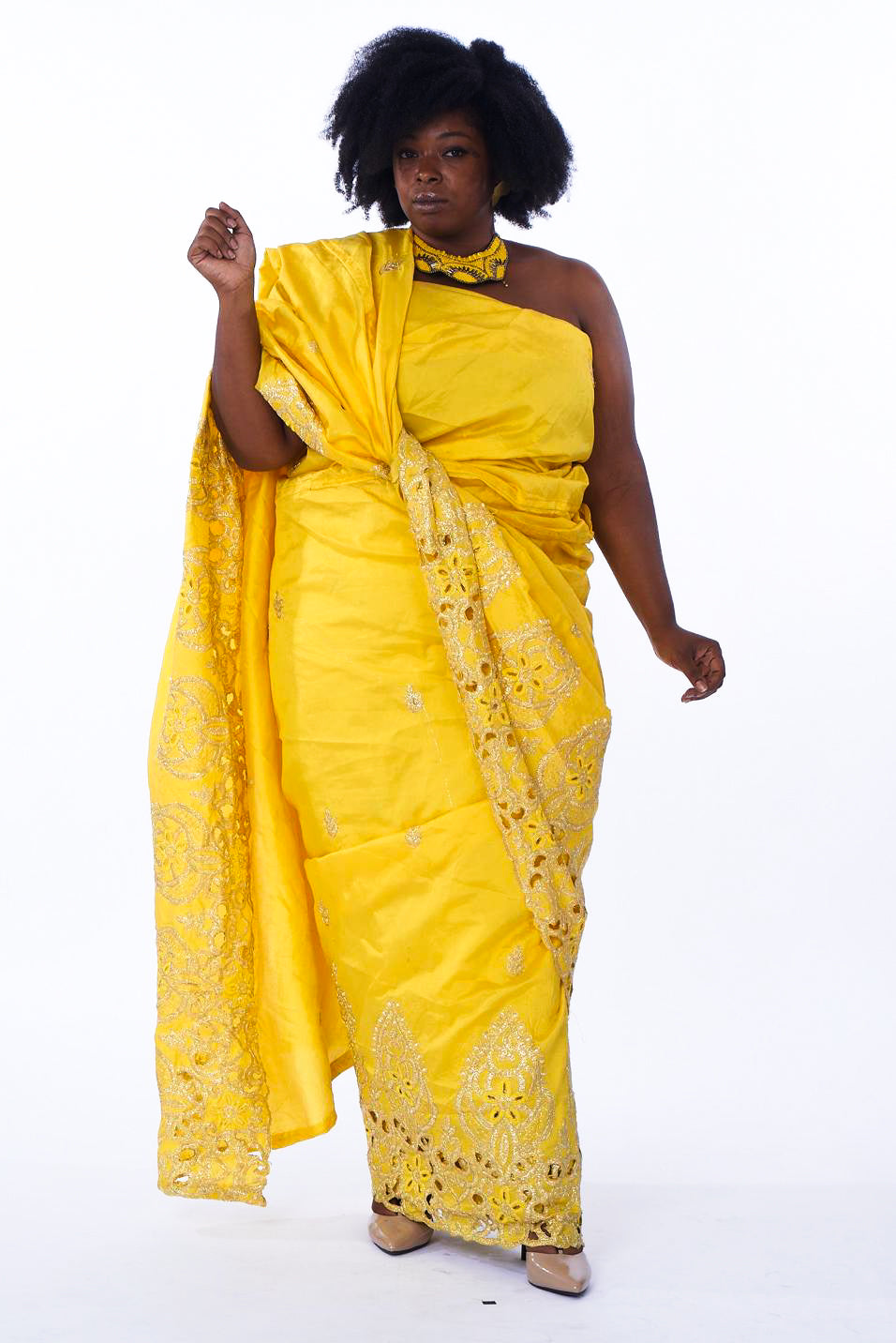 Photo of a woman wearing myObioma's long and yellow Nafrican Dress. The dress features comfortable fabric that is carefully knotted around the waist and thrown over the shoulder. It is imprinted with delicate gold patterns around the hem and across the dress.