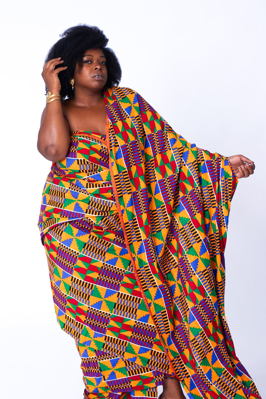 Photo of a woman wearing myObioma's Yaa Fabric Dress, which is loose and multicolored. The dress makes a comfortable fit while the arrangement of abundant geometric shapes and one-sided train makes for free and beautiful movement.