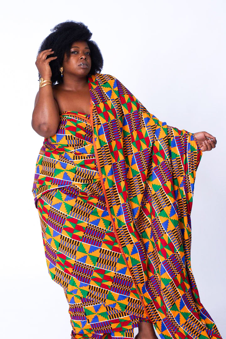 Photo of a woman wearing myObioma's Yaa Fabric Dress, which is loose and multicolored. The dress makes a comfortable fit while the arrangement of abundant geometric shapes and one-sided train makes for free and beautiful movement.