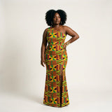 Mgba Kente Ankara one-shoulder floor-length column dress featuring a fitted waist, figure-hugging silhouette, thigh-high side slit, and vibrant yellow, green, red, and black geometric print.