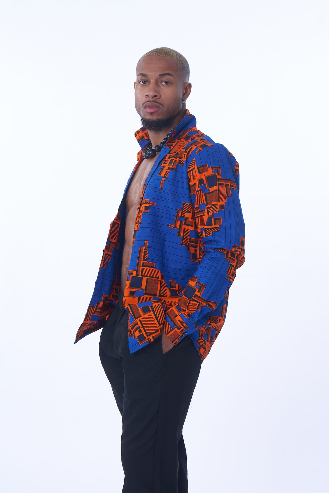 Photo of a man wearing myObioma's bicolor Obi Shirt and Joggers. The open-front shirt is loose and resembles a fancy blazer with a dramatic flared collar. The striking blue shirt features  red prints and long sleeves for a flowery effect. Additionally, the black low-rise joggers include a comfortable elastic waist, pockets, and loose bottoms.