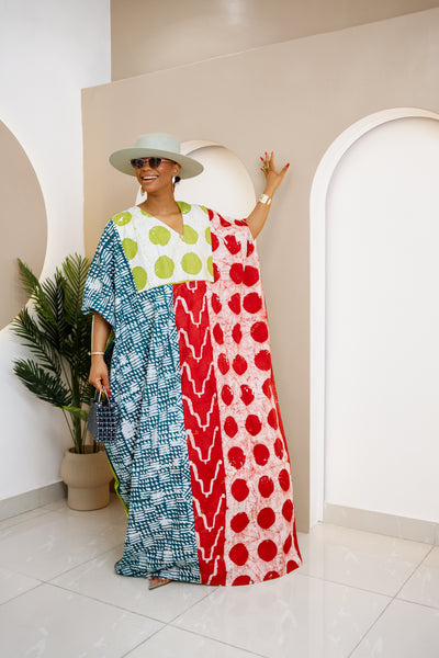 Woman wearing a vibrant, hand-dyed Adire kaftan with geometric and polka dot patterns in blue, red, and green, styled with a chic hat and accessories.