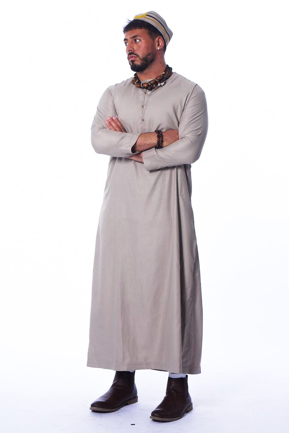 Photo of a man wearing myObioma's long and beige Moroccan Kaftan. The one-piece traditional dress is made with a soft fabric and includes a loose and sheath silhouette for comfort. It features subtle buttons at the upper chest for a simple decorative effect.