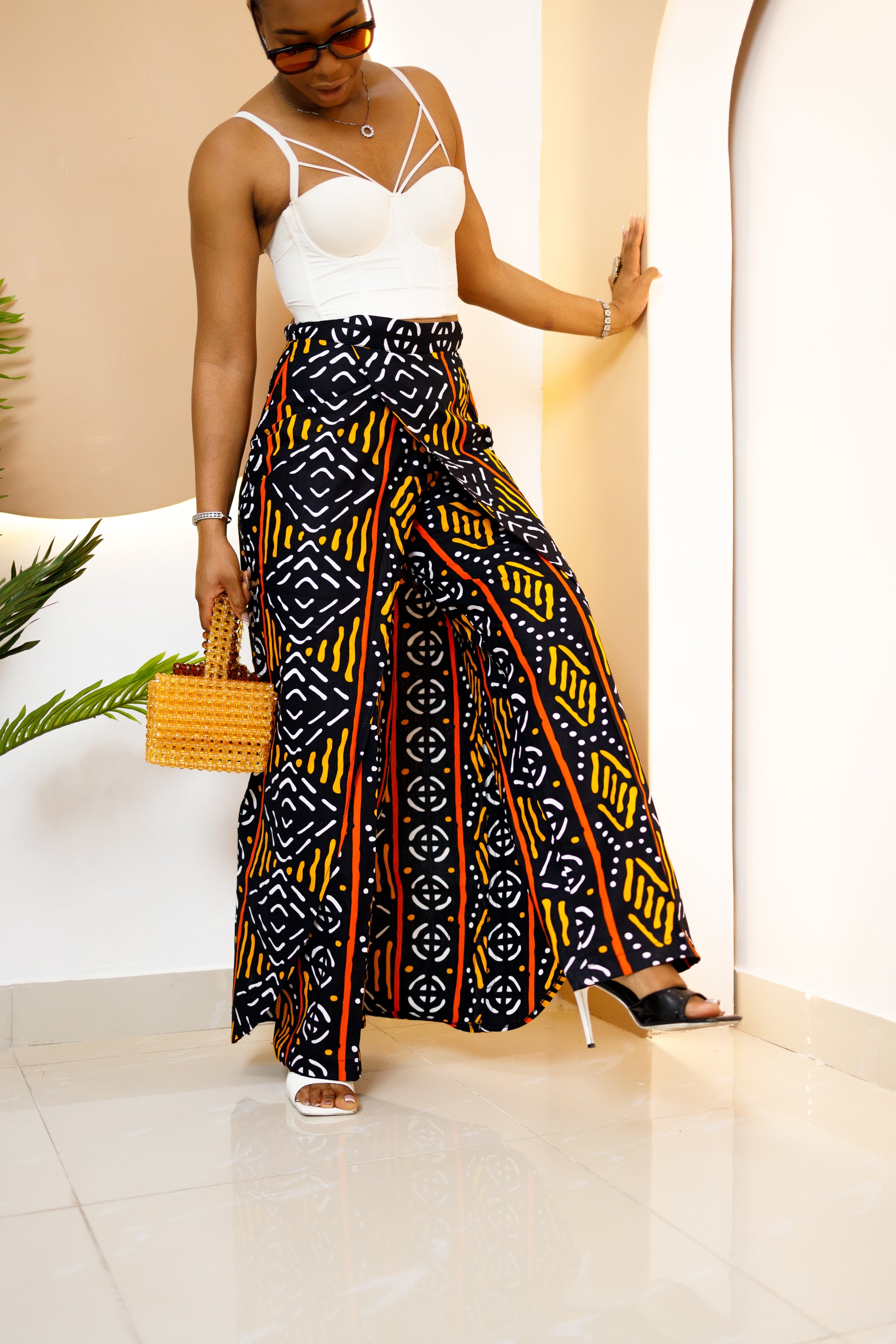 Model wearing a vibrant, multi-colored African Ankara patchwork pants and skirt with intricate patterns, featuring an elastic waistband and zipper closure.