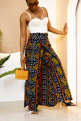 Model wearing a vibrant, multi-colored African Ankara patchwork pants and skirt with intricate patterns, featuring an elastic waistband and zipper closure.