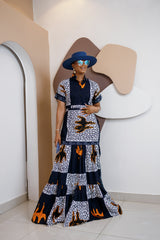 Model wearing Nzama Ankara maxi shirt dress with patchwork print in indigo, white, and orange, styled with a wide-brimmed hat and accessories.