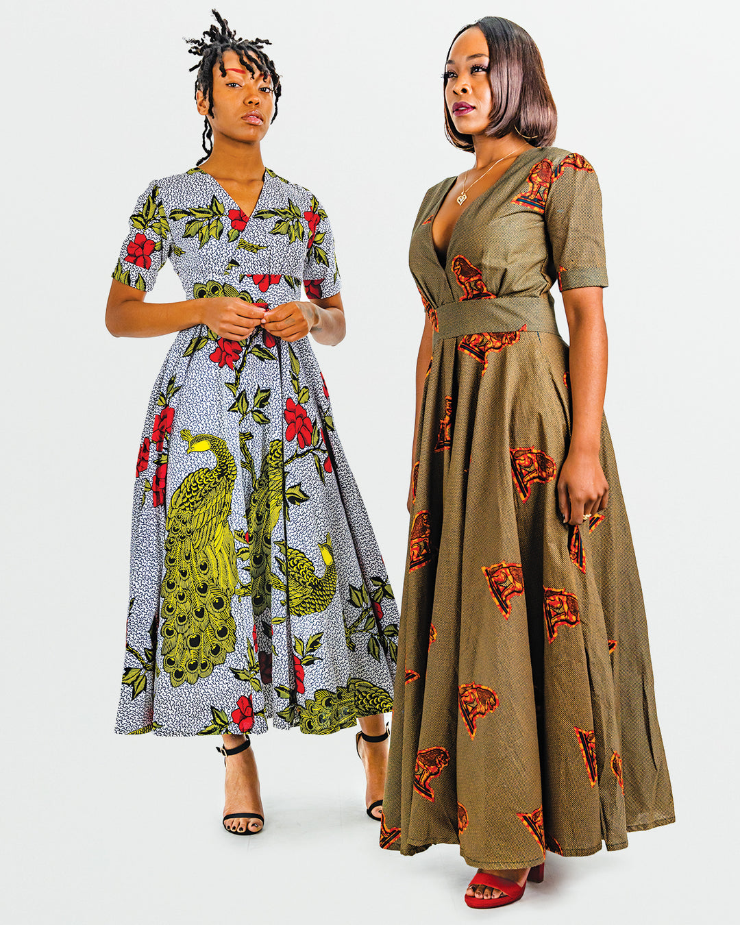 A photo of two women wearing myObioma's Nkechi DRess, which is a African print maxi dress with a v-neck design and a subtle pleated effect from the waist down. It also features a fitted waist design and a zipper on the backside. The fabric is filled dynamic colors and in this photo, one woman wears a peacock and floral print while the other wears a brown and orange print. 