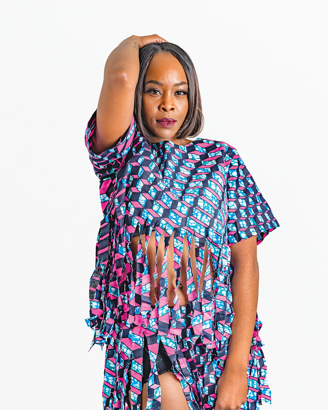 Photo of a woman wearing myObioma's multicolor and bold dancing top. This specific pink and blue dancing top includes a comfortable crew neck feature and loose medium-length sleeves perfect for movement. It also features a gorgeous thick fringe hem that starts under the chest.