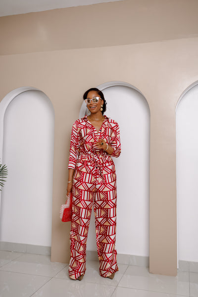 Woman wearing the Onwenwem Silk Jumpsuit with a bold red and white geometric print, accessorized with oversized sunglasses and a red beaded clutch.