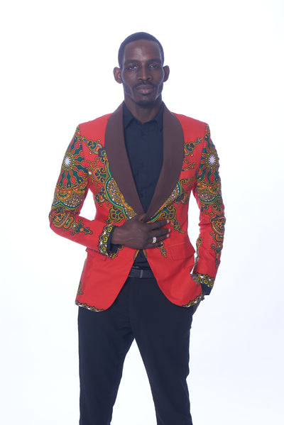 Photo of a man wearing myObioma's red Dashiki Blazer. It features beautiful green and yellow geometric patterns that loop around the sleeves and dark lapels. Classic red flap pockets are included on each side for usage and subtlety as they blend perfectly into the blazer. 