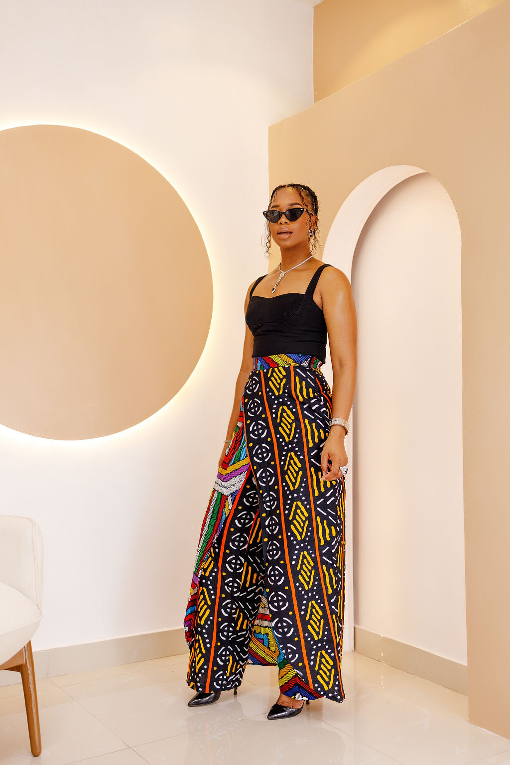 Model wearing a vibrant, multi-colored African Ankara patchwork pants and skirt with intricate patterns, featuring an elastic waistband and zipper closure.