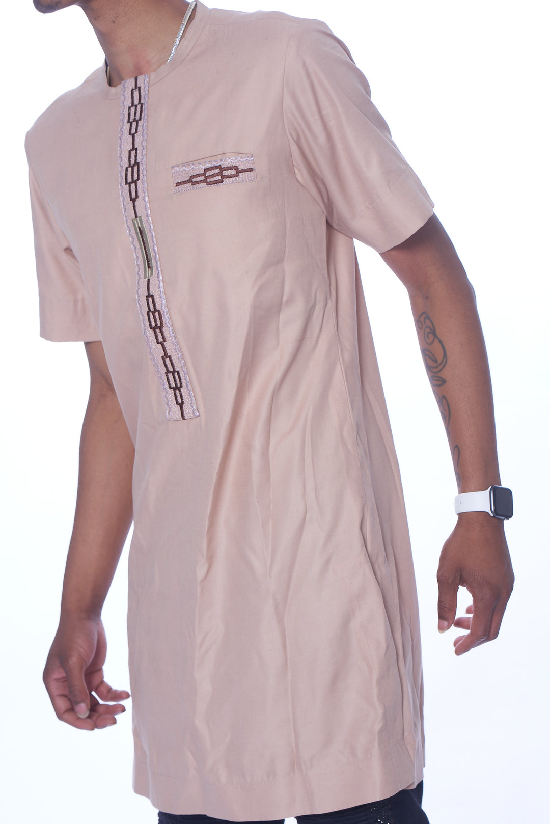 Photo of a man wearing myObioma's Nafrican Kaftan, which is a neutral and beige T-shirt that reaches below the waistline. It includes a crewneck feature and a simple dark brown design pattern resembling a zipper down the chest. There is also a dark brown faux pocket on the upper side of the chest for a decorative effect. 
