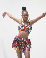 A person wearing a colorful crop top and dancing skirt with frills, posing with arms raised.