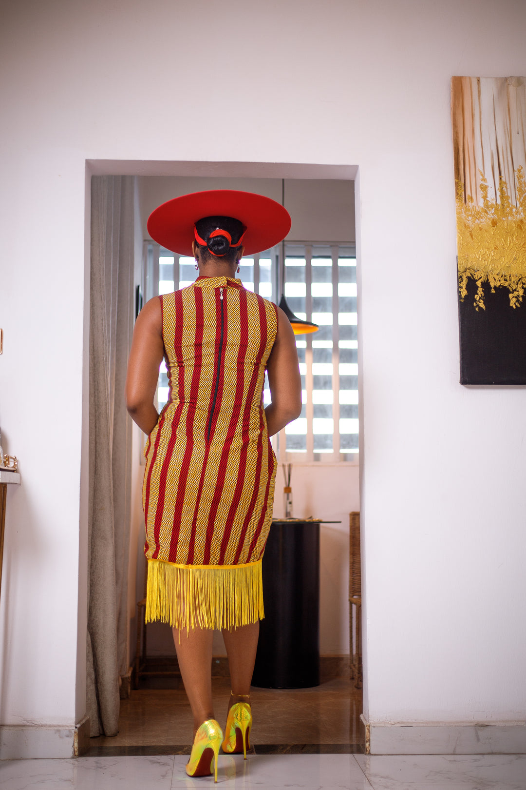 A woman posing in a red and yellow African Ankara print midi dress with frills at the bottom.