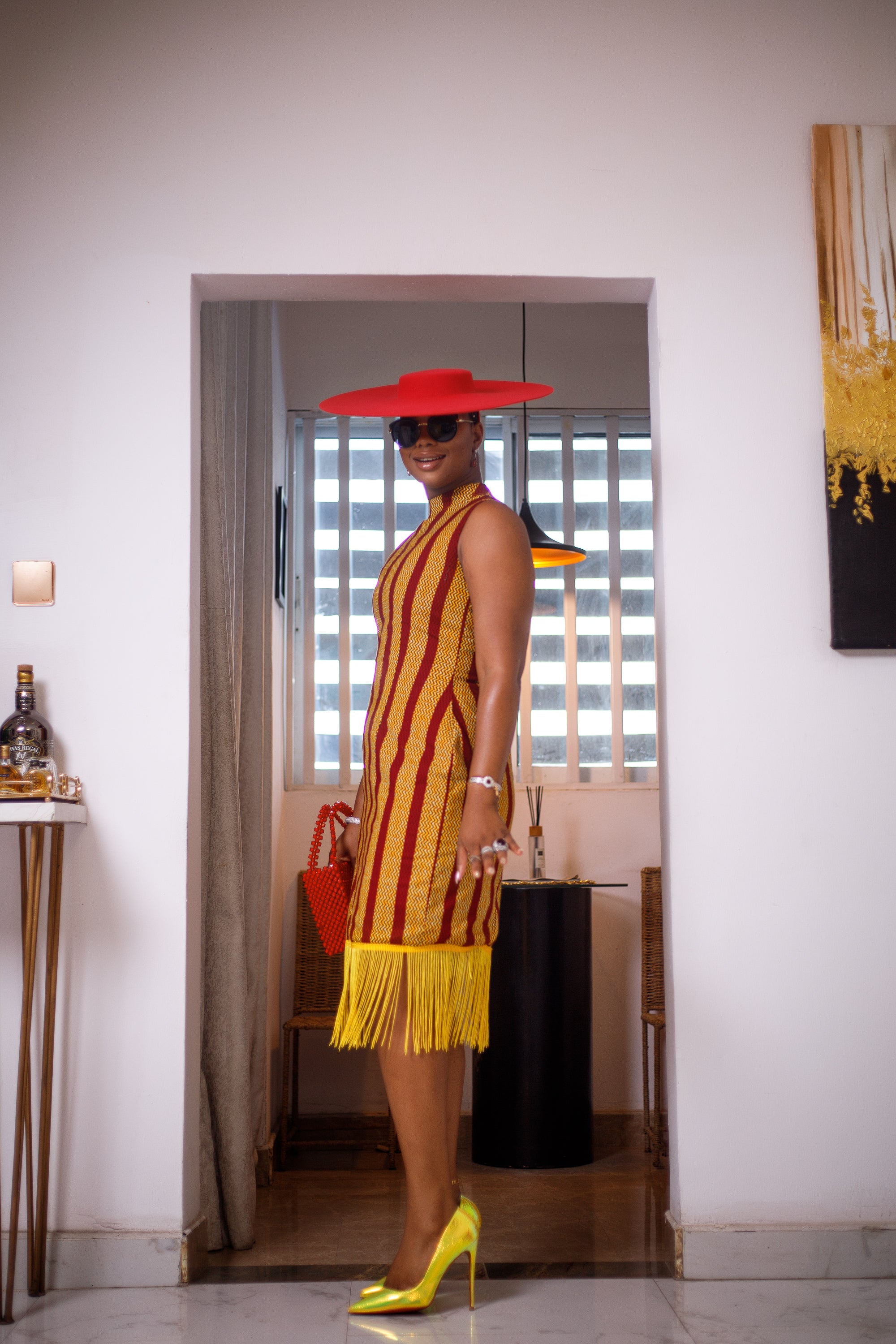 A woman posing in a red and yellow African Ankara print midi dress with frills at the bottom.