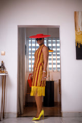 A woman posing in a red and yellow African Ankara print midi dress with frills at the bottom.