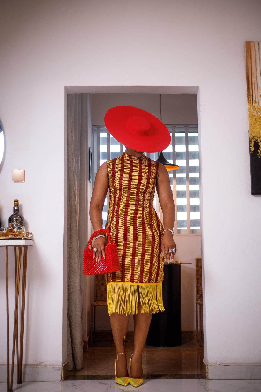 A woman posing in a red and yellow African Ankara print midi dress with frills at the bottom.
