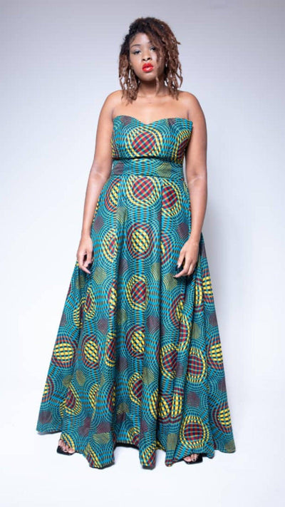 A woman posing in a blue, yellow and purple African print strapless maxi dress. She is pictured facing the camera with her arms at her sides.