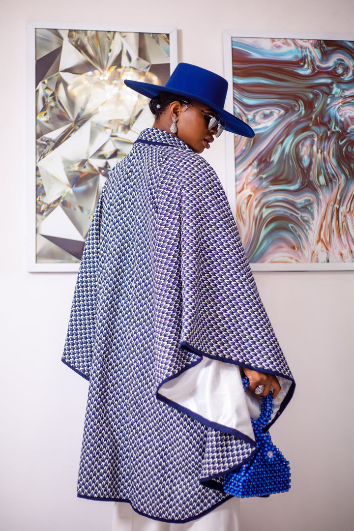A woman posing in a blue and white African Print cape.