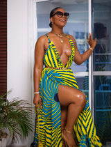 Woman posing in a yellow and blue spiral pattern summer dress. The maxi dress is designed with thin straps, a deep v neckline, and a flattering slit down the right leg.