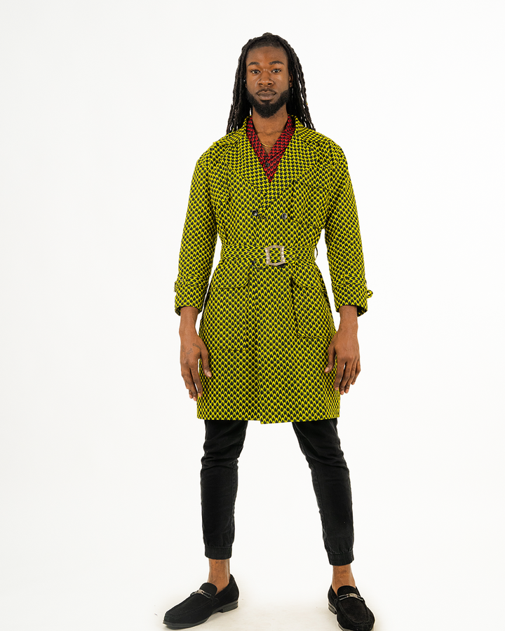 A man posing in a yellow and black African print trench coat.
