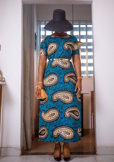 A woman posing in a black and blue African print maxi dress. She is styled with a black sun hat and a mini purse.