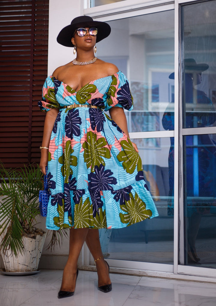 A woman posing in a pink blue and green African Print midi dress.